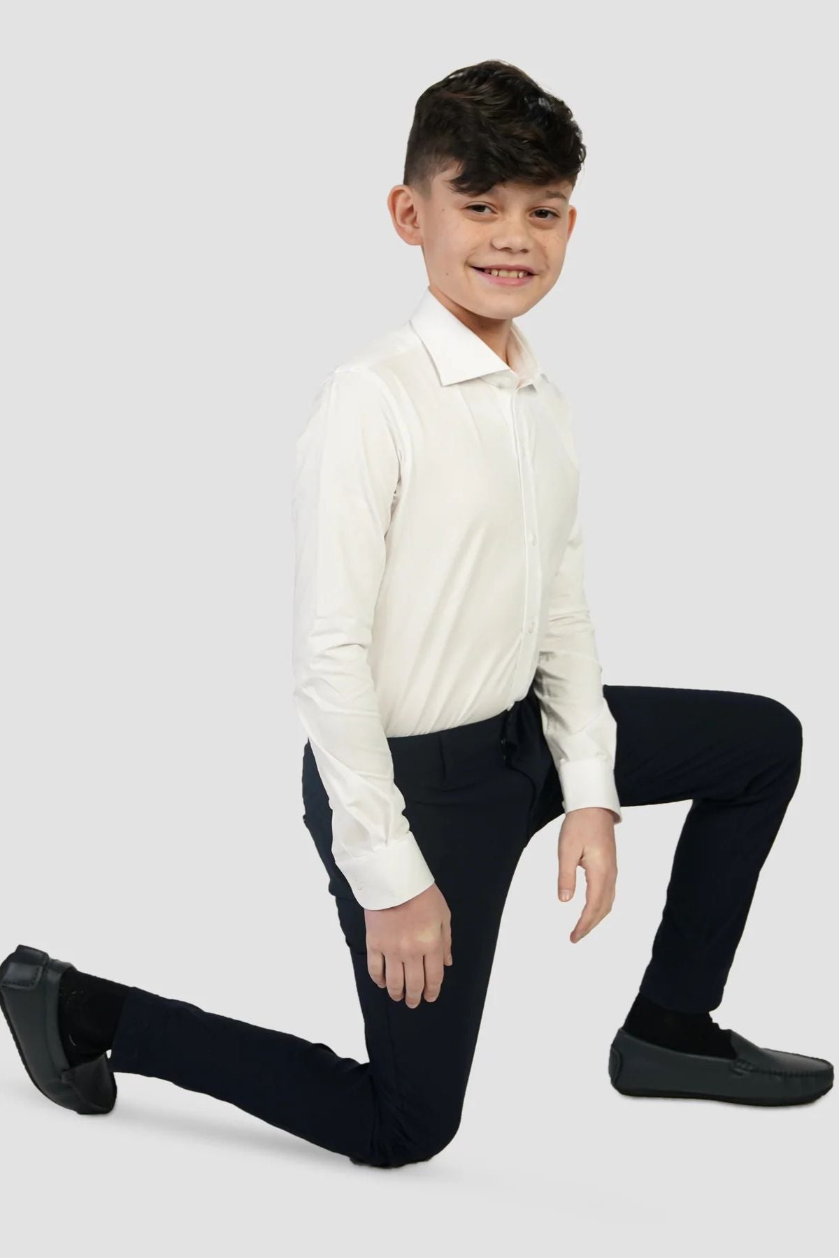 A boy posing with one knee on the ground, wearing a white shirt and navy pants.